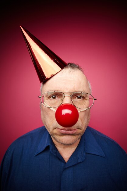 Confused man with red clown nose and birthday hat