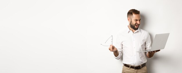 Confused manager looking at laptop standing disappointed against white background