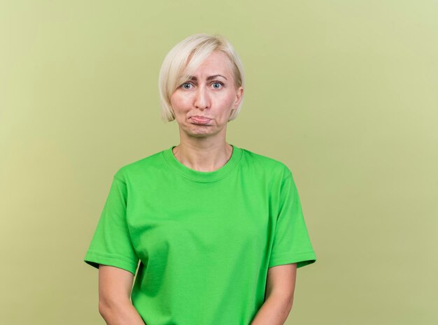 Смущенная блондинка средних лет славянская женщина, смотрящая вперед, изолирована на оливково-зеленой стене с копией пространства