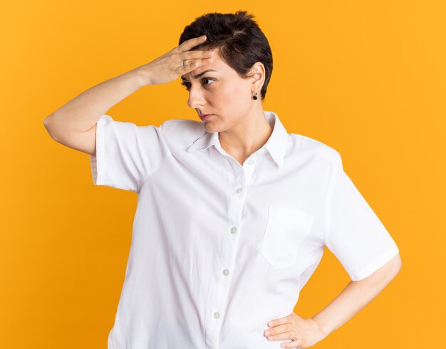 Confused middle-aged woman keeping hands on waist and on head looking at side 