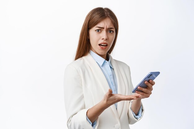 Confused office woman manager complains on smartphone notification reading strange message in app stare puzzled at camera frowning and arguing white background