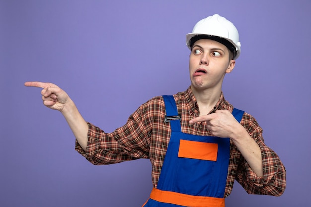 Confused points at side young male builder wearing uniform 