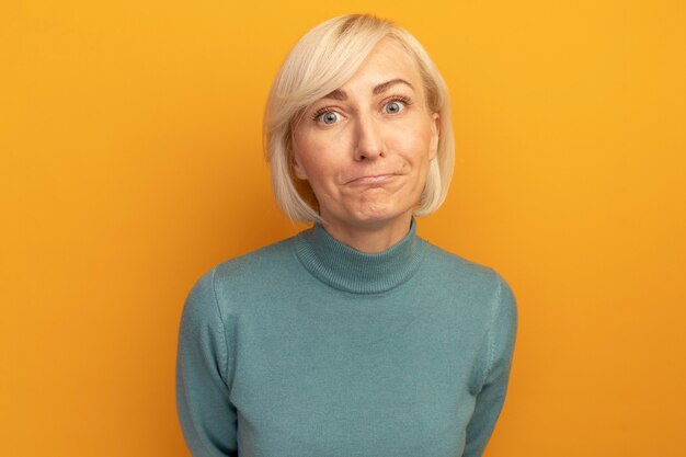 Confused pretty blonde slavic woman looks at front isolated on orange wall