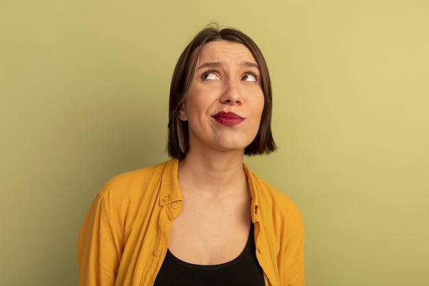 Foto gratuita la donna graziosa confusa esamina il lato isolato sulla parete verde oliva