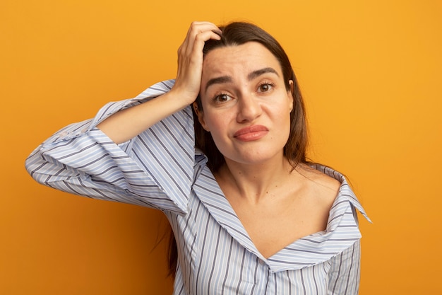 Confused pretty woman puts hand on head isolated on orange wall