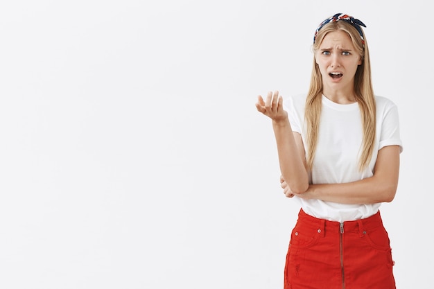 Foto gratuita giovane ragazza bionda confusa e perplessa in posa contro il muro bianco