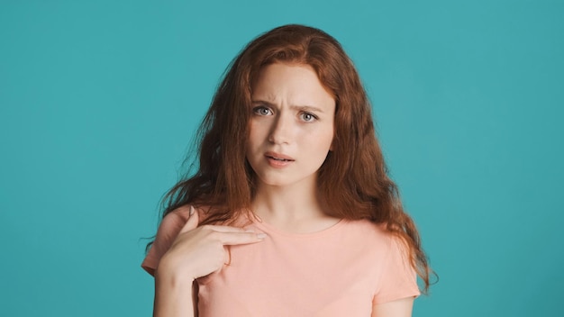 Free photo confused redhead girl pointing finger on herself and showing what expression on camera over colorful background