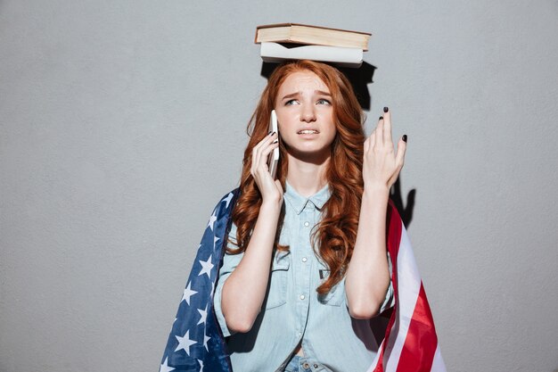 Confused redhead young lady holding book on head