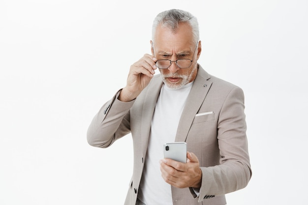 Confused serious-looking elderly businessman looking at mobile phone screen