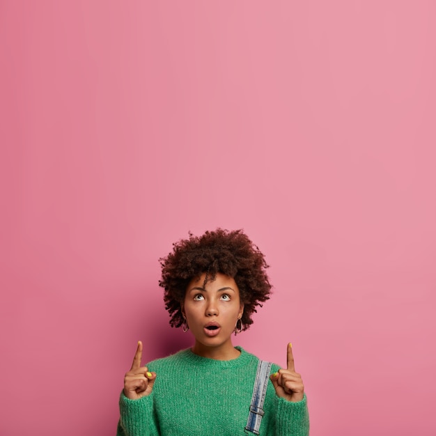 Foto gratuita donna scioccata confusa con acconciatura afro, punta verso l'alto