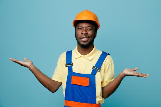 Confused spreading hands young african american builder in uniform isolated on blue background