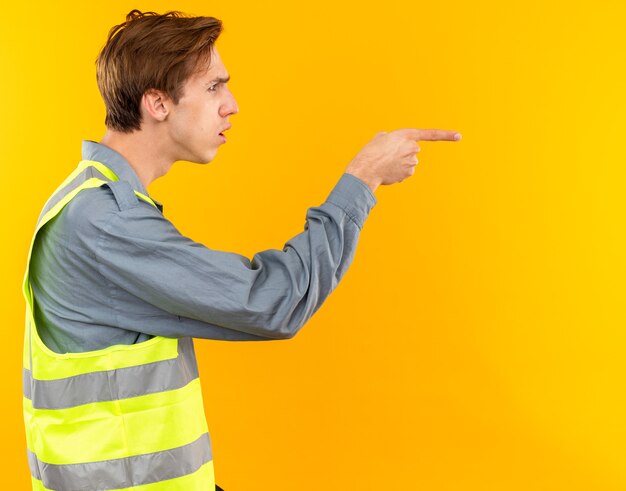 Смущенный стоящий в профиль молодой человек-строитель в форме очков сбоку, изолированный на желтой стене с копией пространства