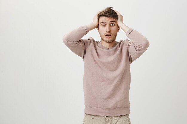 Confused and troubled caucasian guy hold hands on head alarmed