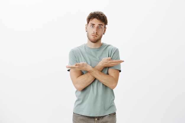 confused and troubled handsome male coworker in trendy t-shirt, crossing hands over chest and pointing left and right, being questioned what direction choose