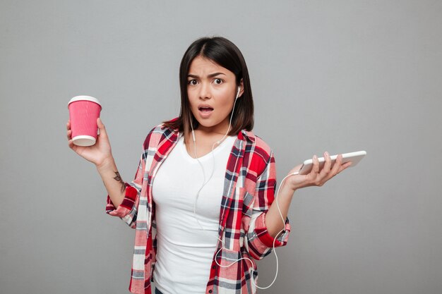 Confused woman holding cup of coffee and listening music.