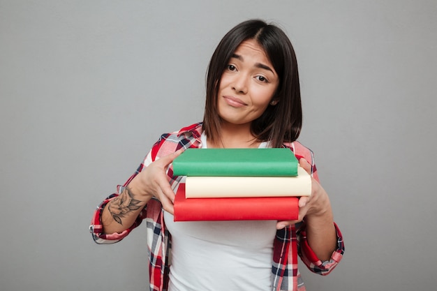 Free photo confused woman holding a lot of books over grey wall