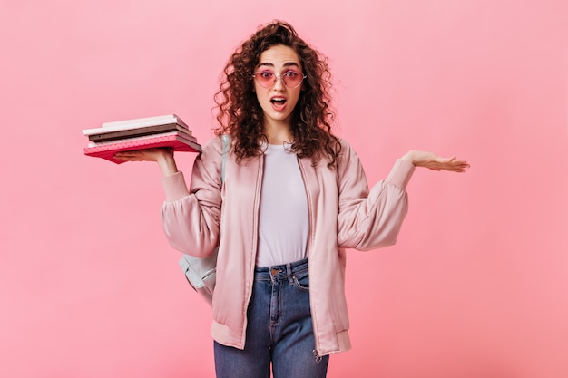 Смущенная женщина в розовом наряде держит книги и позирует на изолированном фоне