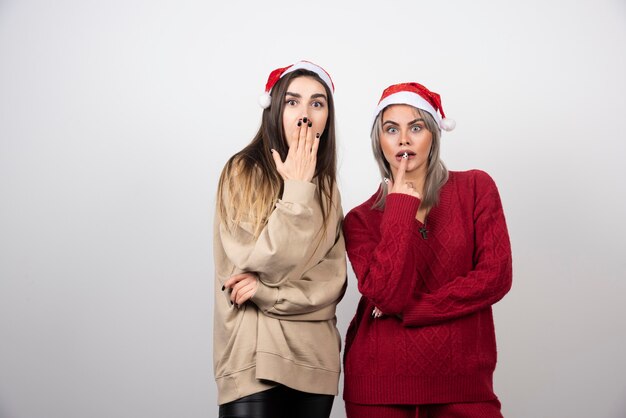 confused women friends posing isolated over white wall.