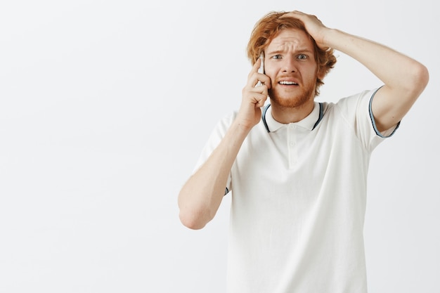 Confused and worried bearded redhead guy posing against the white wall