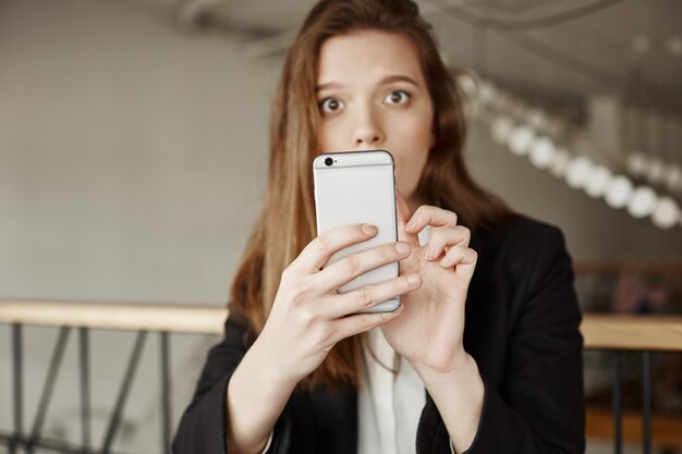 Confused worried woman looking at you while using mobile phone