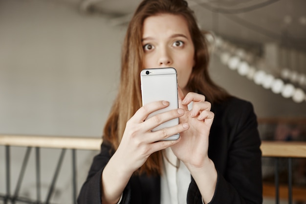 Confused worried woman looking at you while using mobile phone