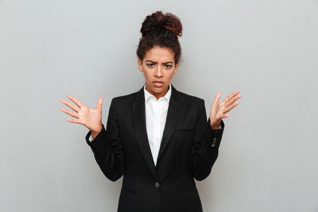 Confused young african business woman standing over grey wall