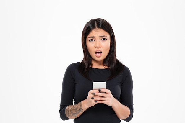 Confused молодая азиатская женщина беседуя по мобильному телефону