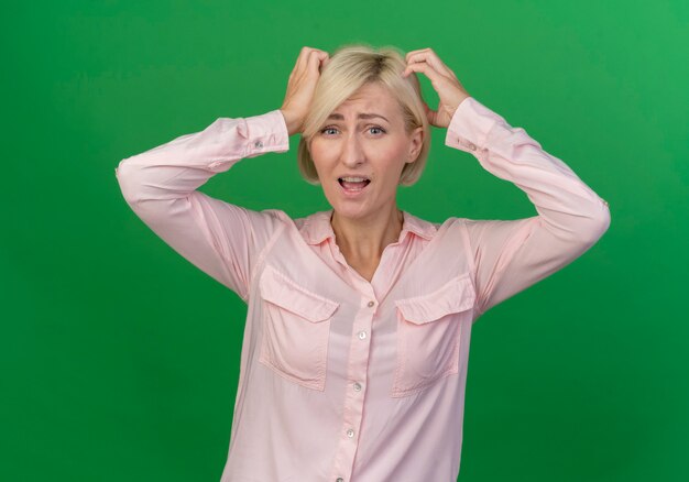 Confused young blonde slavic woman touching head with hands isolated on green background