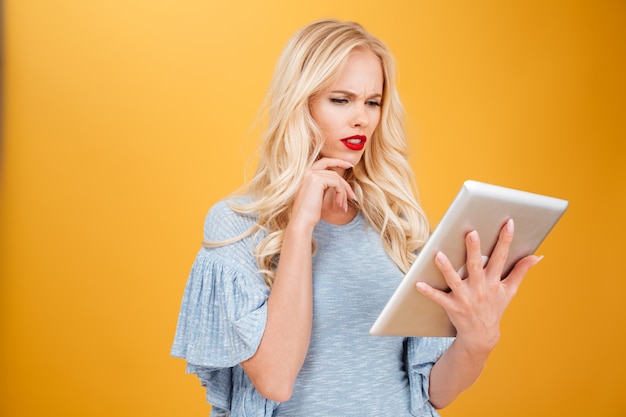 Confused young blonde woman using tablet computer.