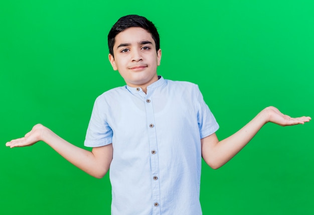 Confused young boy showing empty hands looking at front isolated on green wall