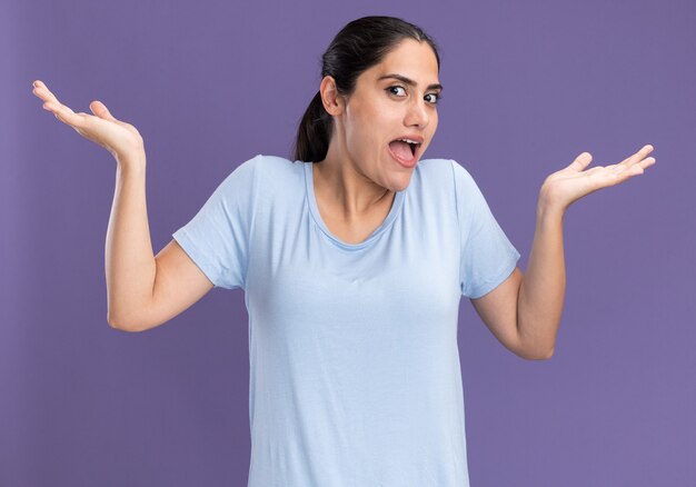 Confused young brunette caucasian girl holding hands open on purple