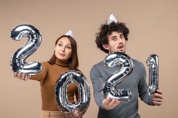 Confused young couple wear new year hat poses for camera Girl showing and and guy with and on gray