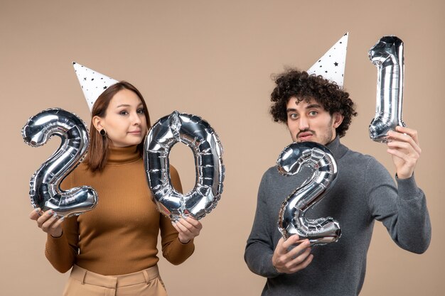 Confused young couple wear new year hat poses for camera Girl taking and guy with and on gray