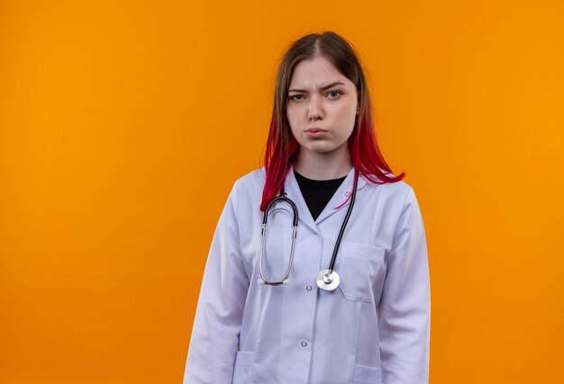 격리 된 오렌지 벽에 청진 의료 가운을 입고 혼란 된 젊은 의사 여자