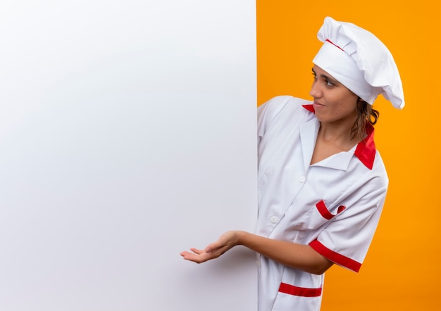Foto gratuita confuso giovane cuoco femminile che indossa la tenuta uniforme dello chef e guardando la parete bianca sulla parete gialla isolata con lo spazio della copia