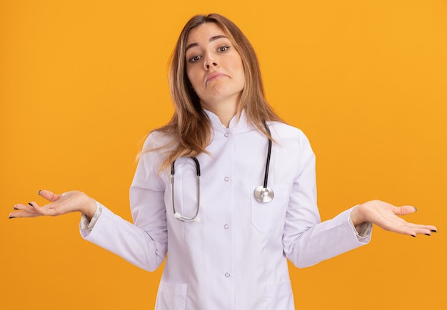 Free photo confused young female doctor wearing medical robe with stethoscope spreading hands isolated on yellow wall