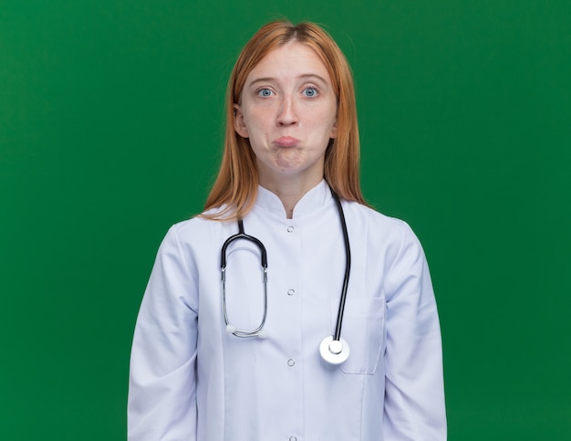 Confused young female ginger doctor wearing medical robe and stethoscope 