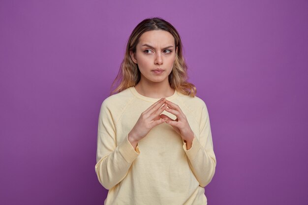 Confused young girl keeping hands together looking at side 