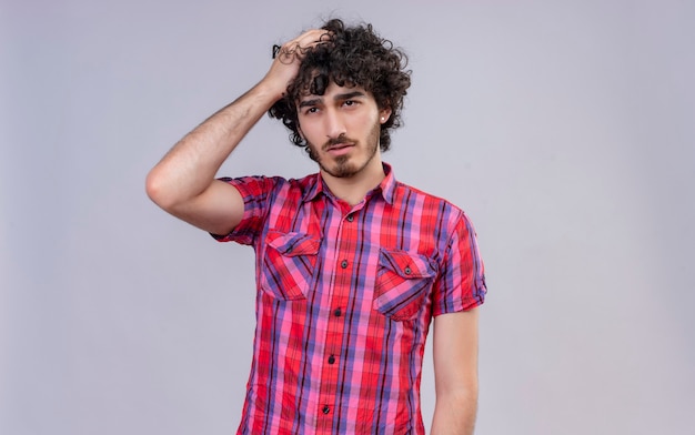 A confused young good-looking man with curly hair in checked shirt holding hand on hair 