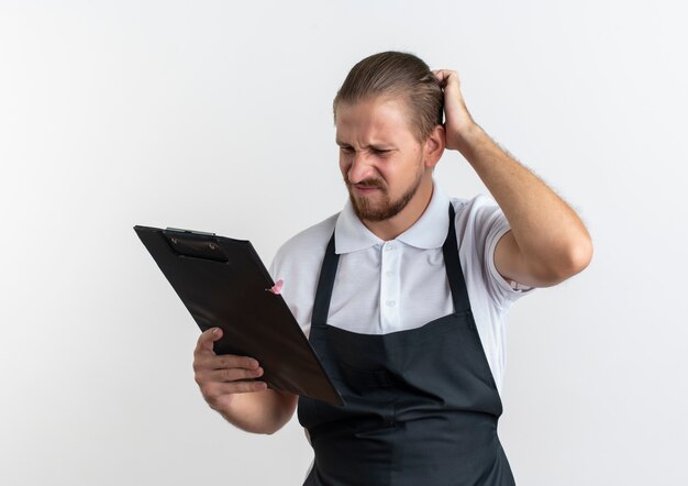 制服を着て、白で隔離の頭に手でクリップボードを見て混乱した若いハンサムな理髪師