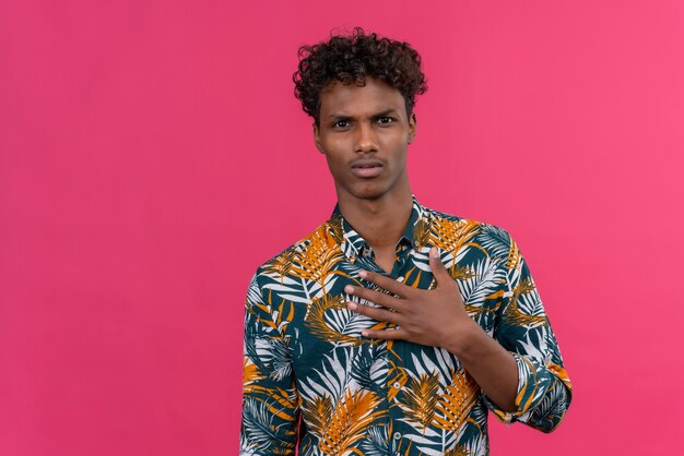 Confuso giovane bell'uomo di pelle scura con i capelli ricci in camicia stampata foglie che punta a se stesso chiedendo che mi riferisci