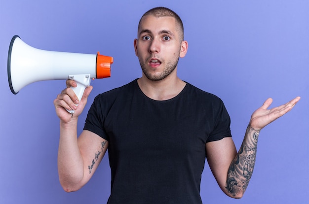 Confuso giovane bel ragazzo che indossa t-shirt nera con altoparlante isolato su sfondo blu