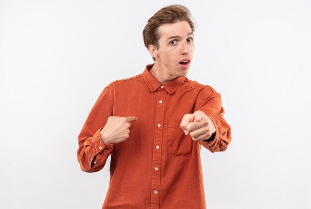 Смущенный молодой красивый парень в красной рубашке указывает на себя, показывая вам жест