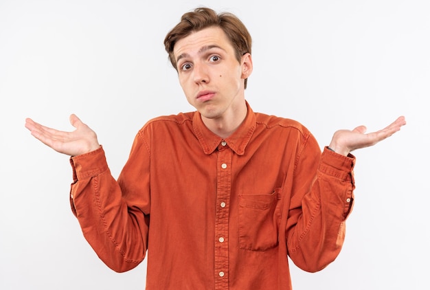 Confused young handsome guy wearing red shirt spreading hands 