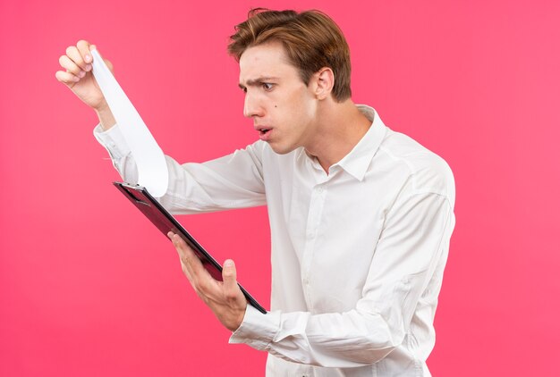 Confused young handsome guy wearing white shirt holding and looking at clipboard 