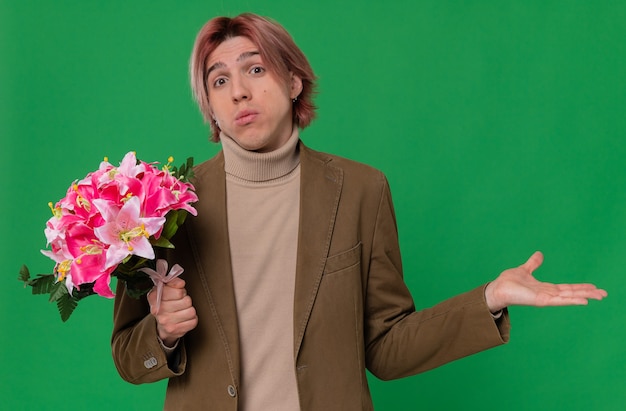 Confused young handsome man holding bouquet of flowers and keeping his hand open 
