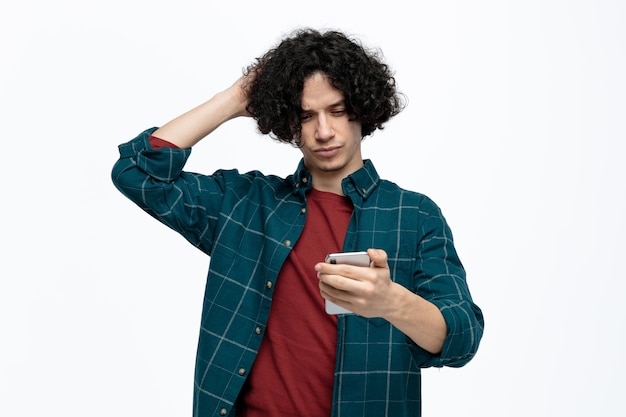 Free photo confused young handsome man holding and looking at mobile phone scratching head isolated on white background