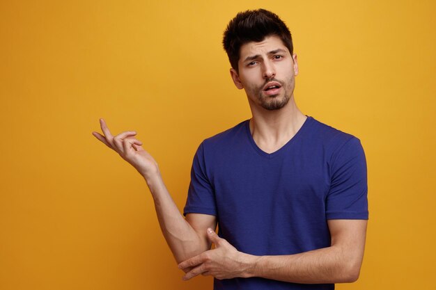Confused young handsome man looking at camera pointing to side on yellow background