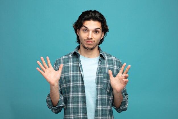 confused young handsome man looking at camera showing empty hands isolated on blue background