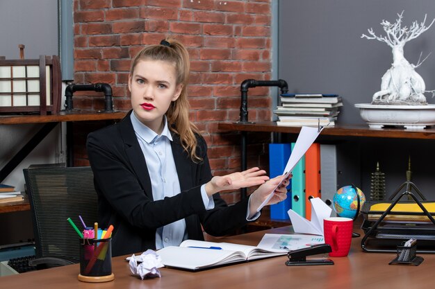 Confused young lady sitting at a table and showing the document in the office